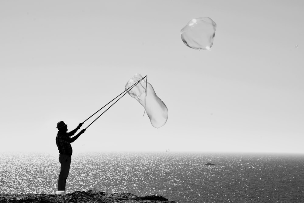man holding stick making bubbles beside body of water