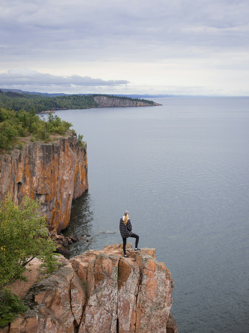昼間、水辺の崖の上に立つ女性