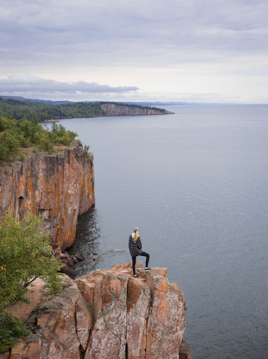 woman standing on cliff near body of water during daytime in Tettegouche State Park United States