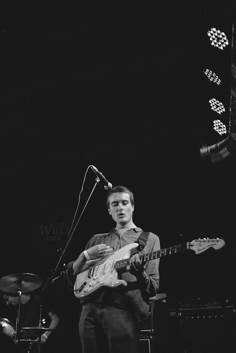 grayscale photography of man playing guitar on stage