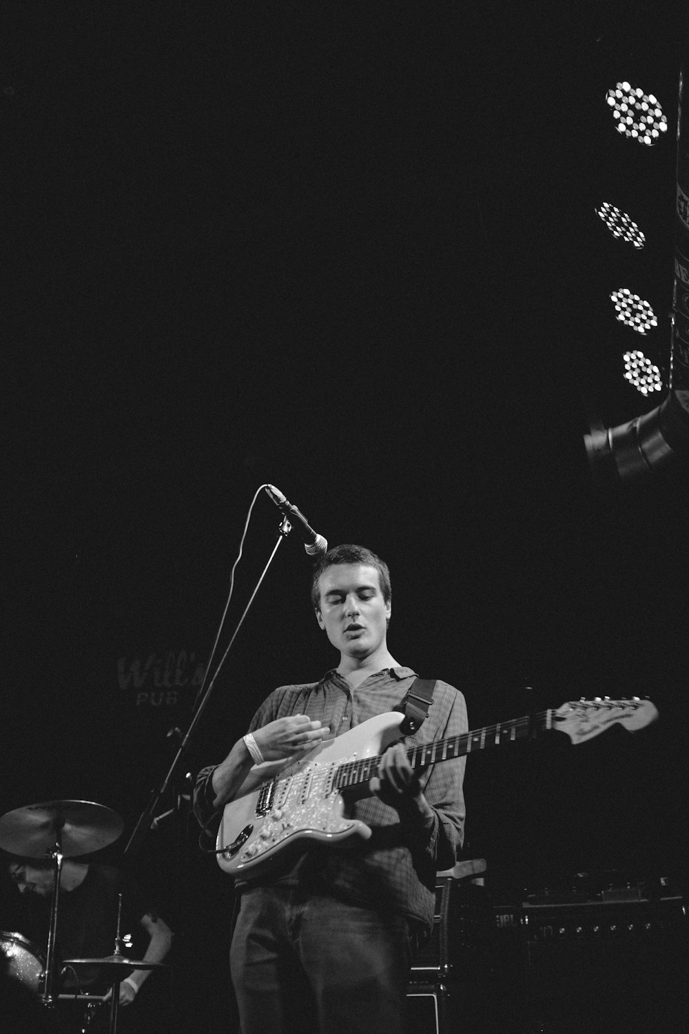 grayscale photography of man playing guitar on stage