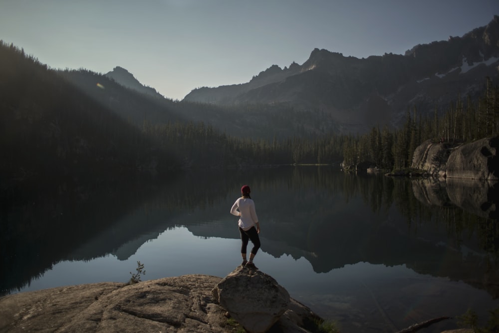 person standing on cliff near lake