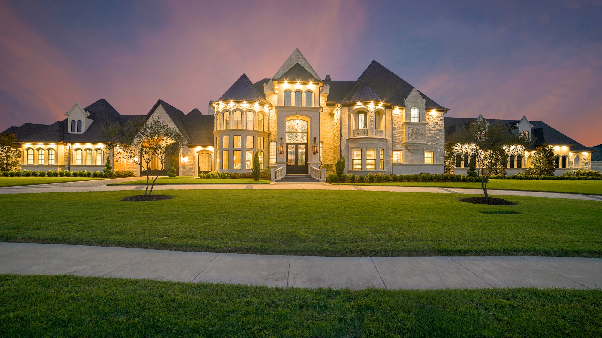 Brick estate home lit warmly at dusk behind a broad lawn