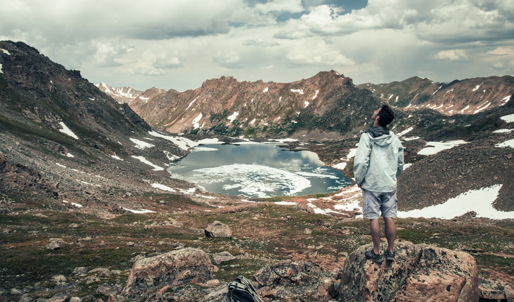 man standing facing at lake surround by mountains