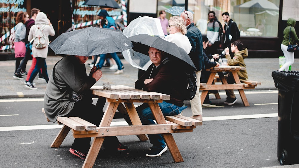 검은 우산 아래 갈색 피크닉 테이블에 앉아있는 두 남자