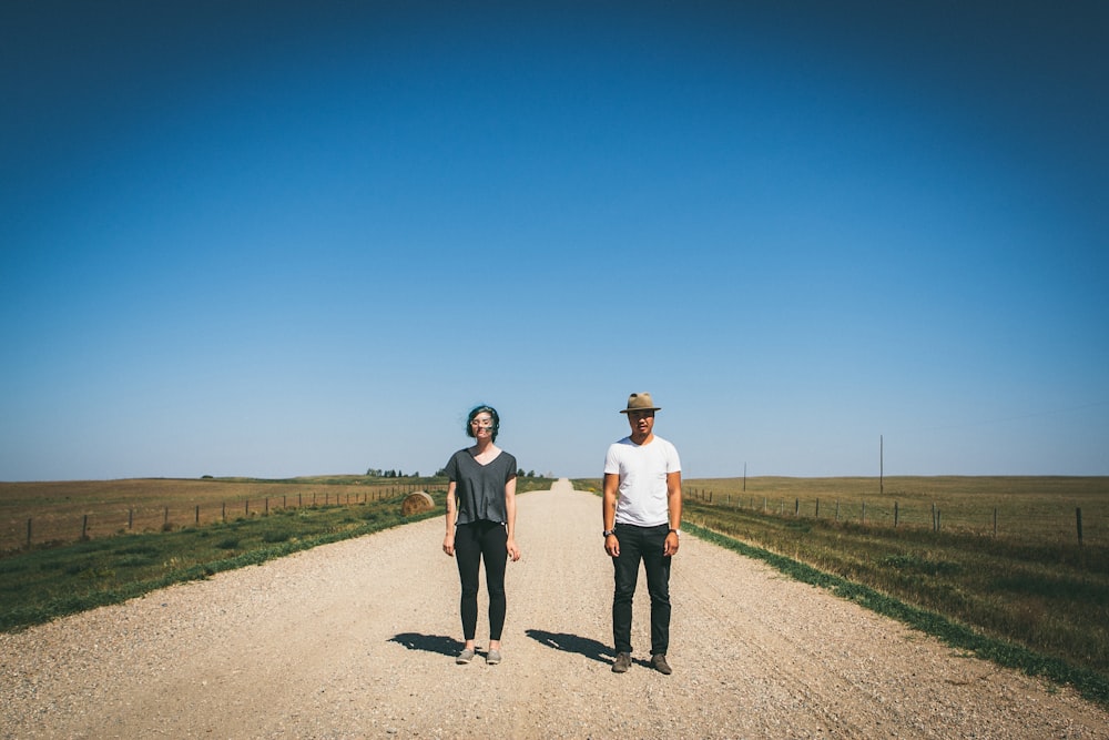 man and woman standing on road between grass fields during daytime