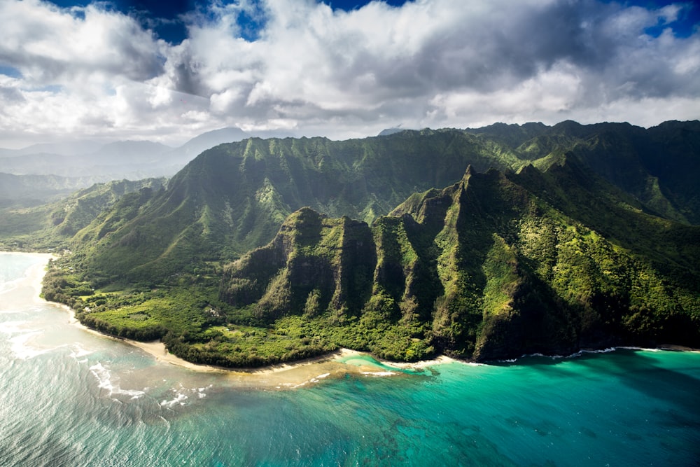 aerial photography of green mountain beside body of water under white sky