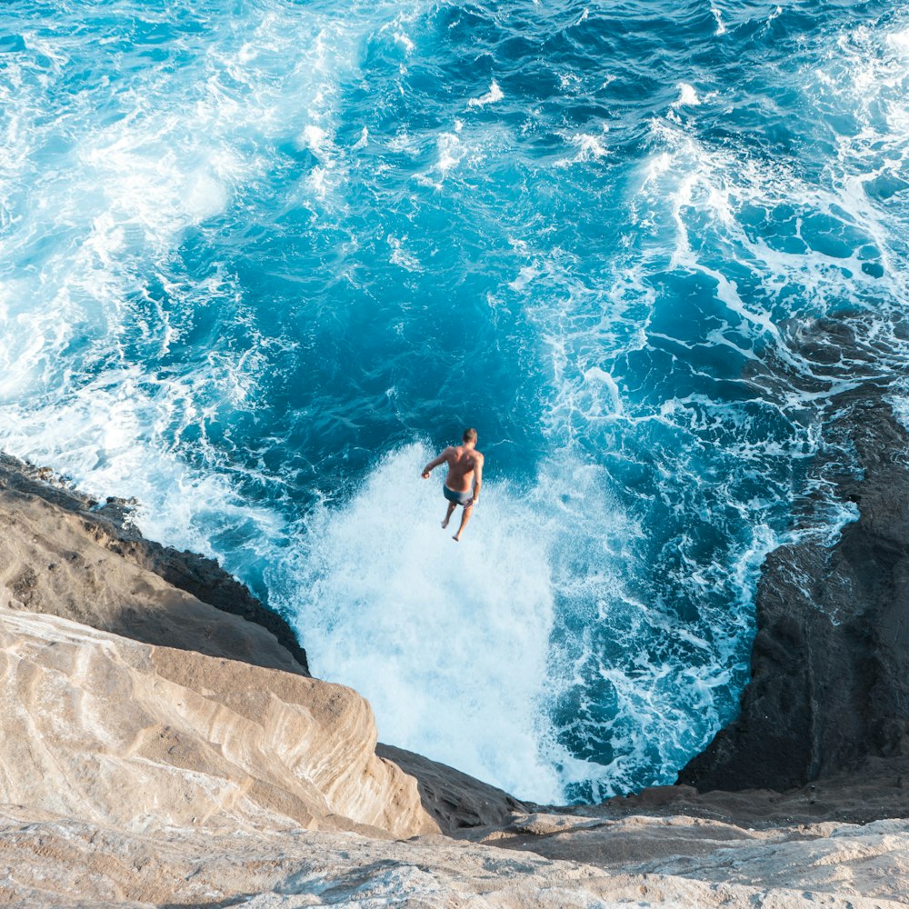 aerial photo of man jumping on cliff to the water