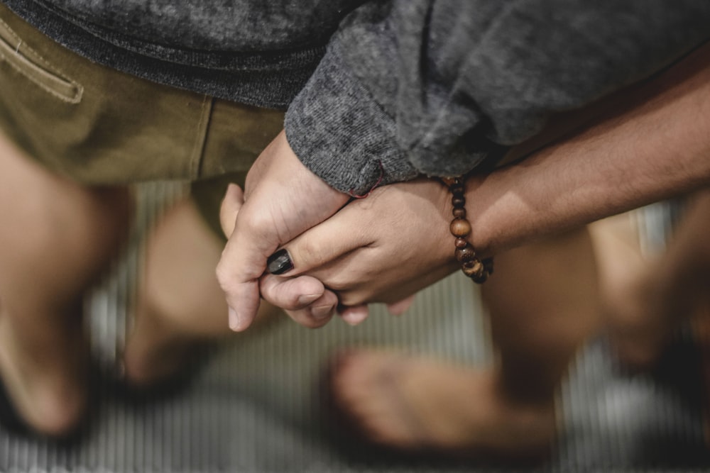 two person holding hands selective focus photography