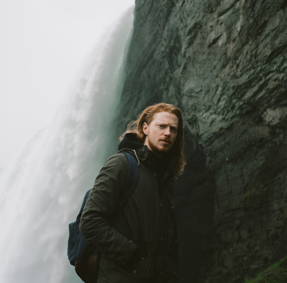 man in black jacket standing beside rock formation