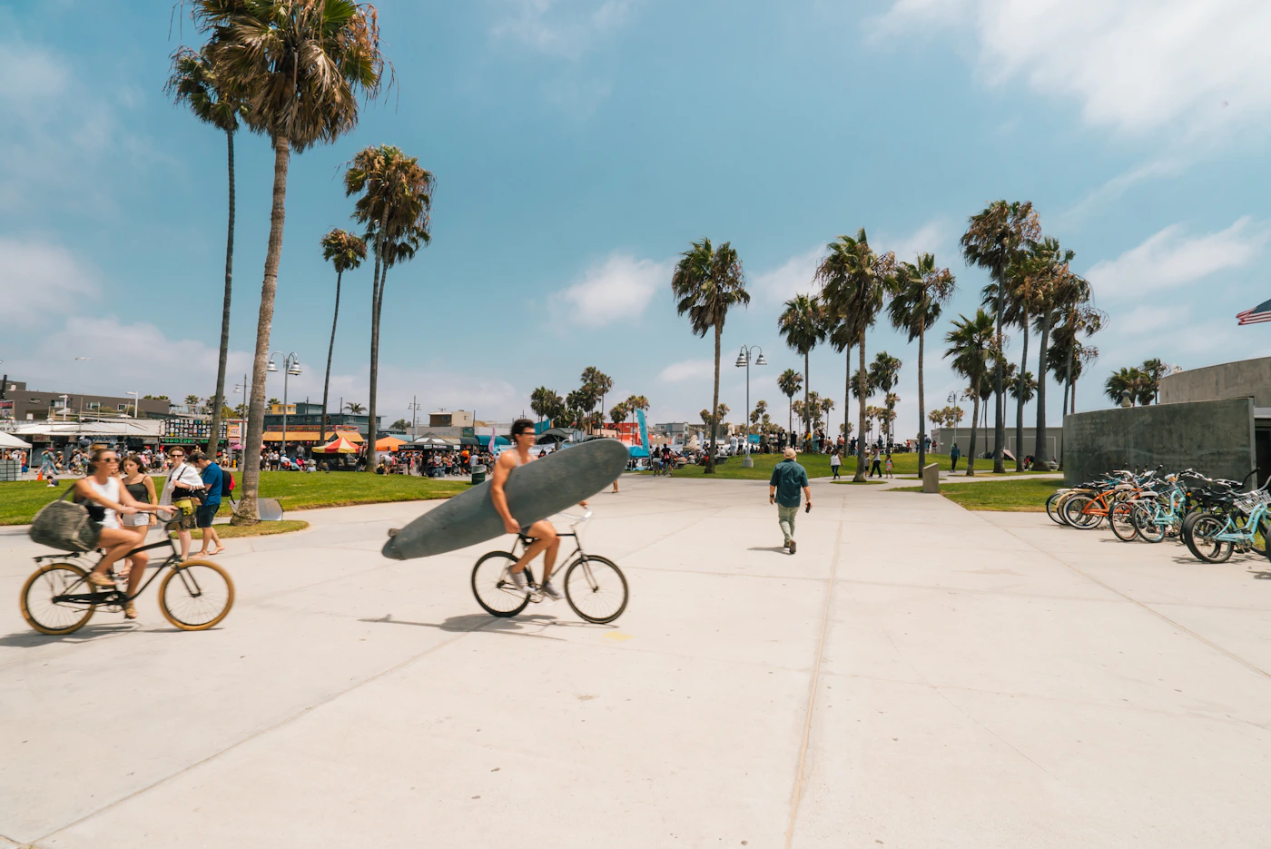 Man carrying surfboard on bicycle along Venice Beach — The Strand beachfront path
