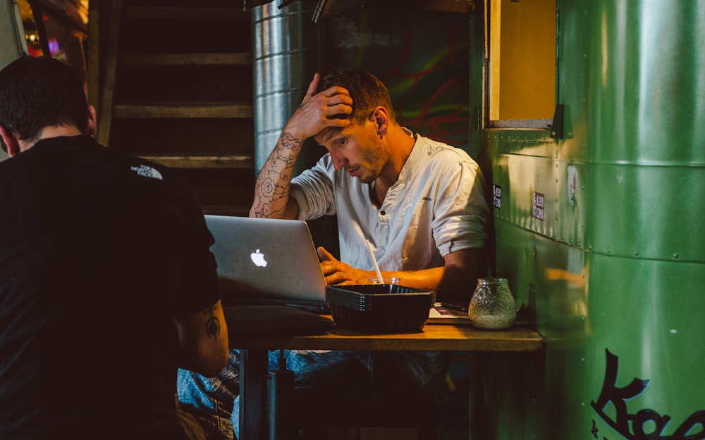 uomo di fronte al MacBook d'argento mentre si gratta la testa