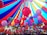 A vibrant array of colorful balloons is gathered under a large, multi-colored canopy. The balloons come in shades of red, pink, blue, purple, and green, floating upwards and filling the space under the tent. The canopy itself features bold stripes of red, blue, and yellow, creating a festive and lively atmosphere.
