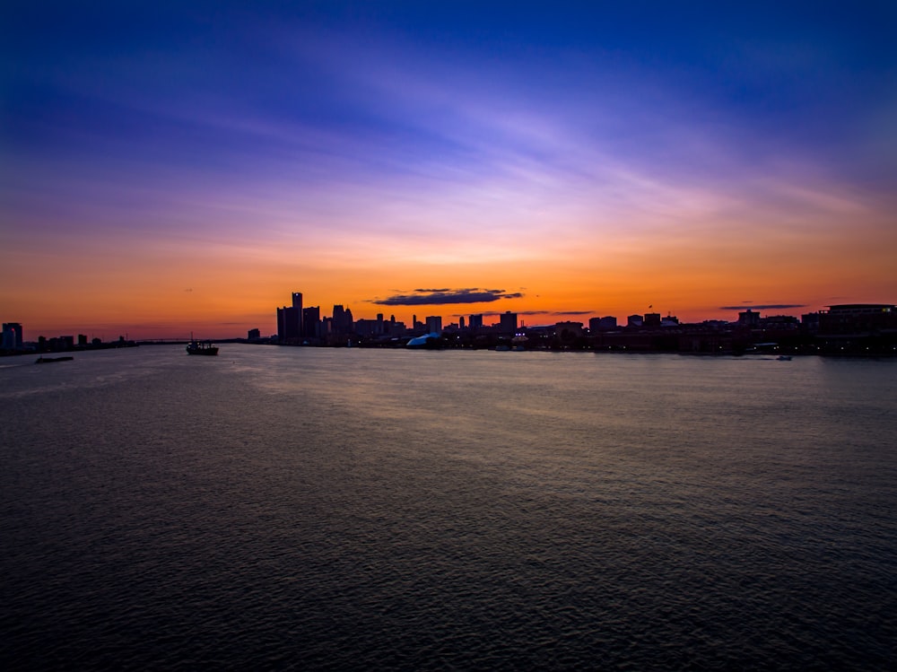 silhouette of city buildings and boat above water at golden hour