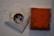 A dirty and worn-out electrical socket is mounted on a wall, next to a rusty, square metal plate with a reddish-brown surface.