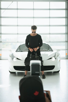 Portrait of Azedine Aboukamel standing confidently beside a sleek car in a bright showroom.