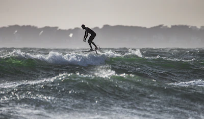 Close-up of a sleek efoil board cutting through gentle waves with a backdrop of Formentera’s coastline.
