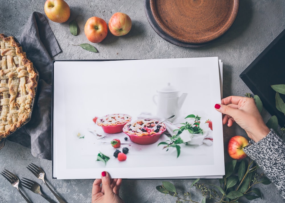 person holding painting beside apples