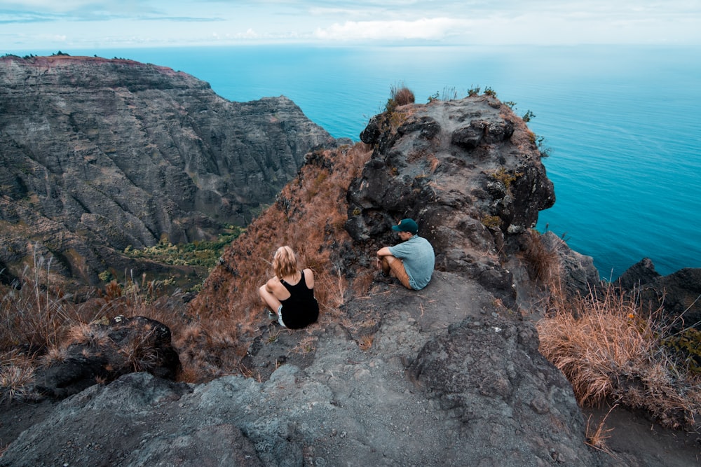 homme et femme assis sur la montagne pendant la journée