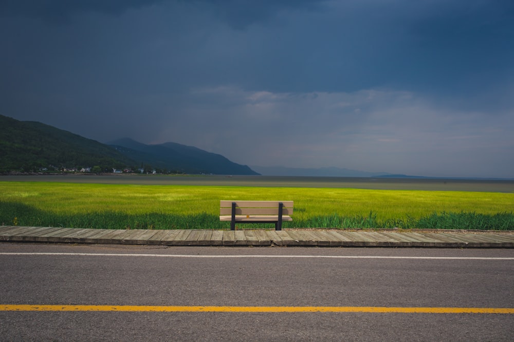beige wooden bench near green rice field under blue and white sky during daytime