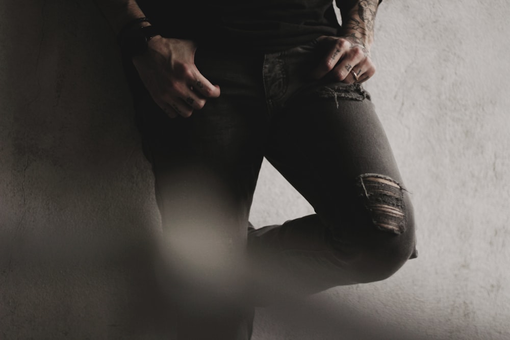uomo che indossa jeans neri angosciati appoggiati al muro di cemento