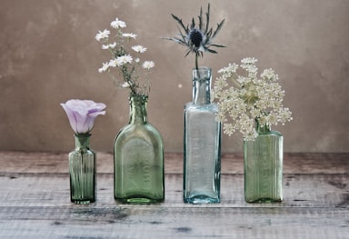 three green and one blue glass vases with flowers inside