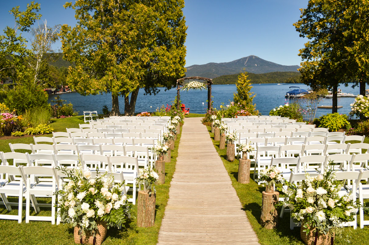 An outdoor ceremony with white chairs and flowers beside a mountain lake