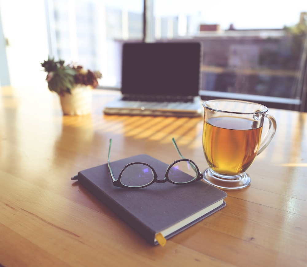 clear eyeglasses on top of black book beside clear glass mug