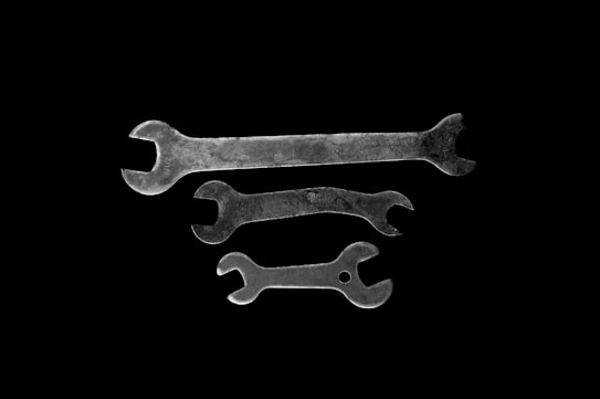 Three metal wrenches of varying sizes are arranged against a black background. The wrenches have a vintage, worn appearance with some visible rust and patina.