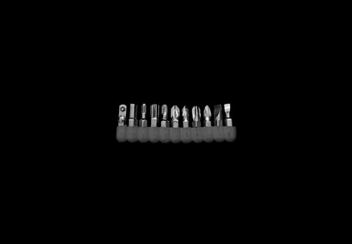 A set of metal screwdriver bits neatly lined up in a holder against a black background, showcasing different types of tips for various screws.