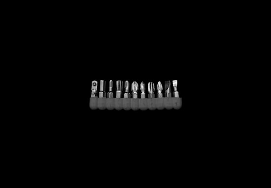 A set of metal screwdriver bits neatly lined up in a holder against a black background, showcasing different types of tips for various screws.