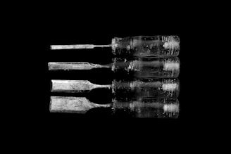 Four well-worn chisels with transparent handles arranged in a horizontal line against a solid black background. The blades vary slightly in size and exhibit signs of significant use and wear.