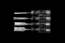 Four well-worn chisels with transparent handles arranged in a horizontal line against a solid black background. The blades vary slightly in size and exhibit signs of significant use and wear.