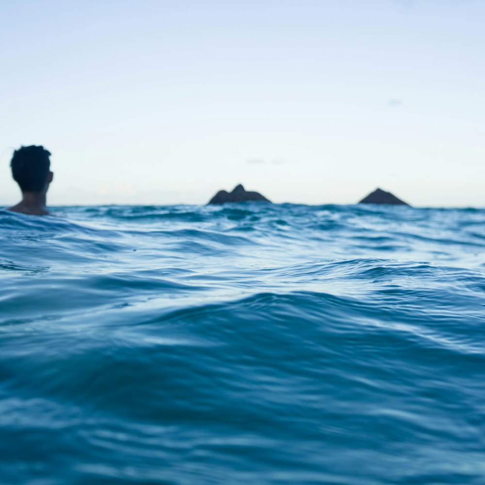 man swimming on body of water during daytime