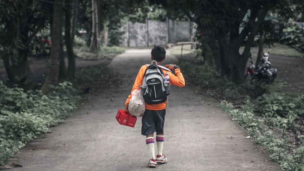 boy with backpack walking on pathway between trees