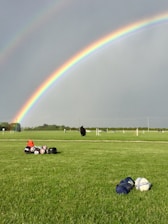 A vibrant softball flying over a rainbow-colored field under a clear blue sky.