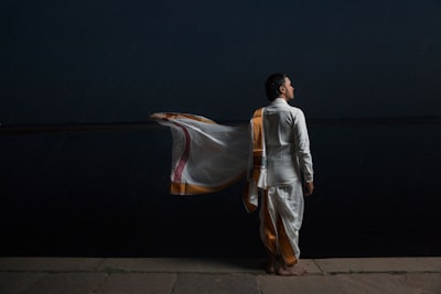 man in white and brown traditional dress standing beside black wall evening teams background