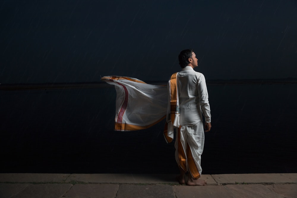 man in white and brown traditional dress standing beside black wall