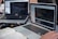 Two laptops displaying code are placed on a desk. One laptop is a Dell, and the other is a MacBook. Both screens show some programming code in a development environment. There is also a notebook with handwritten notes, a mouse, and a smartwatch on the table. A person is typing on the MacBook.