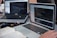 Two laptops displaying code are placed on a desk. One laptop is a Dell, and the other is a MacBook. Both screens show some programming code in a development environment. There is also a notebook with handwritten notes, a mouse, and a smartwatch on the table. A person is typing on the MacBook.