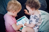 two toddlers sitting on sofa while using tablet computer