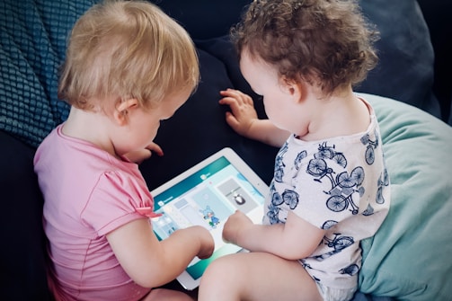 two toddlers sitting on sofa while using tablet computer