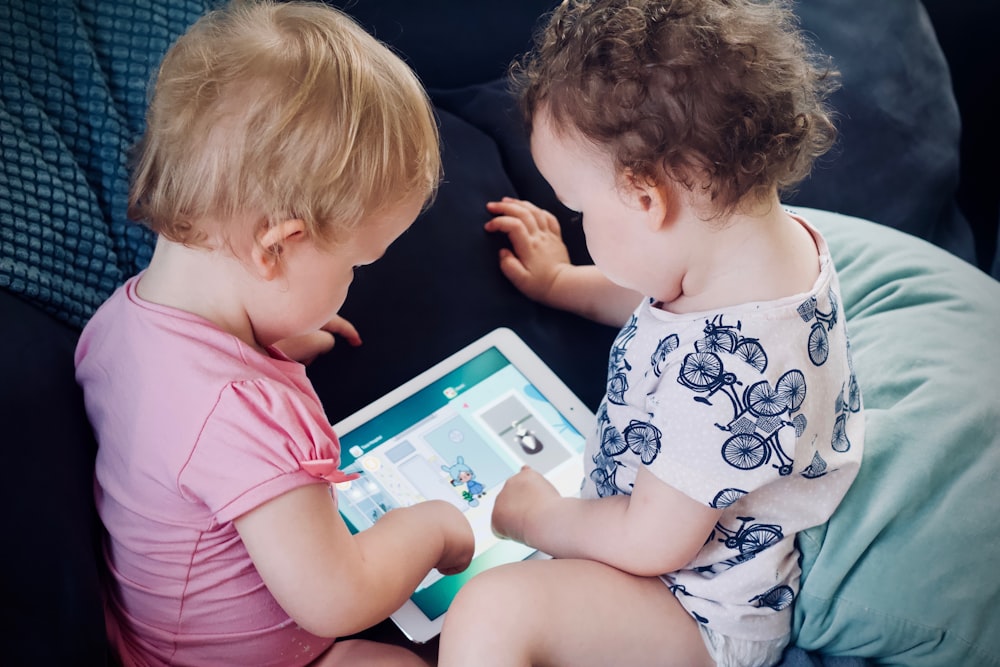 zwei Kleinkinder sitzen auf dem Sofa, während sie einen Tablet-Computer benutzen