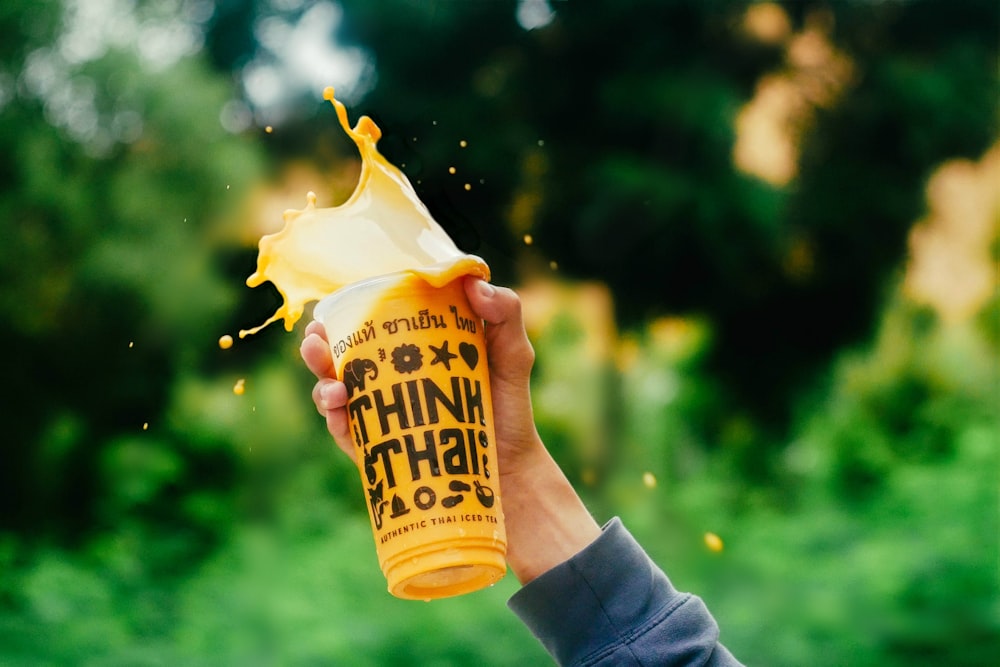 person holding Think Thali disposable cup with beverage spilling out