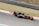 A Formula 1 car is racing on a track, featuring visible branding and logos such as Renault. The vehicle is painted in a combination of orange and black, and the image captures the motion and speed of the car. The background consists of grass and track barriers, slightly blurred due to the car's movement.