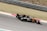 A Formula 1 car is racing on a track, featuring visible branding and logos such as Renault. The vehicle is painted in a combination of orange and black, and the image captures the motion and speed of the car. The background consists of grass and track barriers, slightly blurred due to the car's movement.