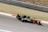 A Formula 1 car is racing on a track, featuring visible branding and logos such as Renault. The vehicle is painted in a combination of orange and black, and the image captures the motion and speed of the car. The background consists of grass and track barriers, slightly blurred due to the car's movement.