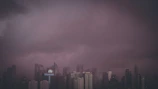 A dark cityscape with towering futuristic buildings under a stormy sky.