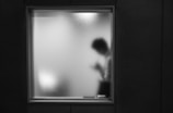A blurred silhouette of a person standing behind a frosted window, suggesting mystery and privacy. The figure appears to be engaging with something in their hands, possibly a smartphone.