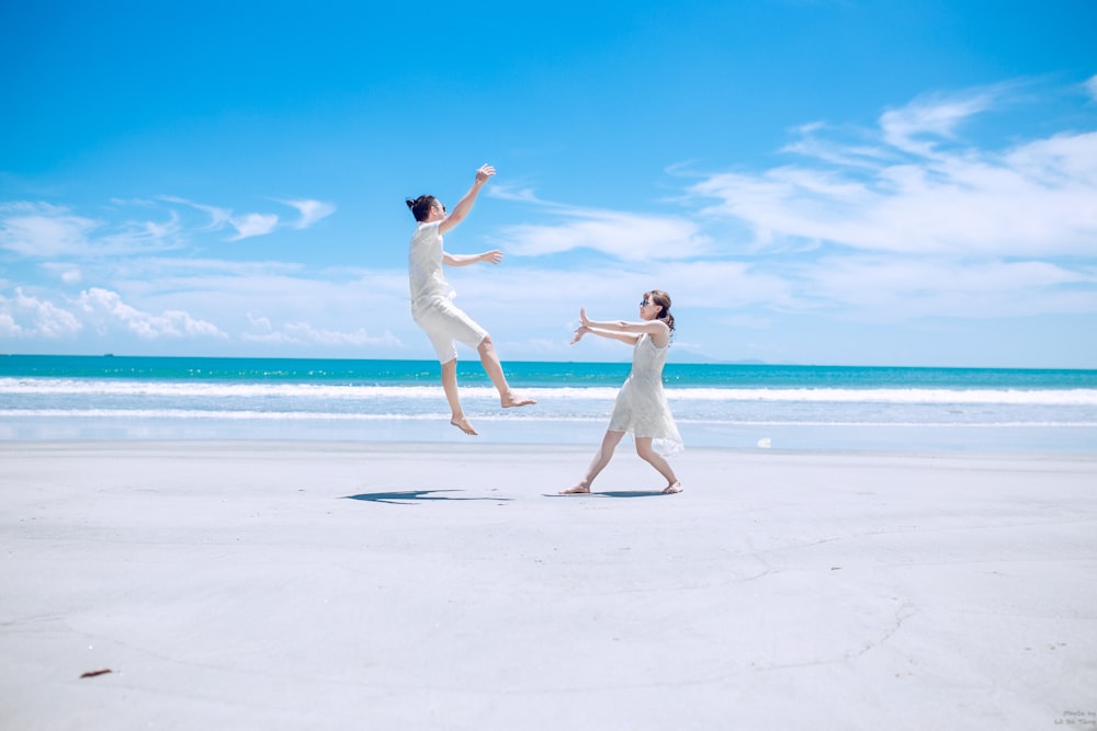 Mann und Frau spielen tagsüber auf weißem Sand in der Nähe der Küste
